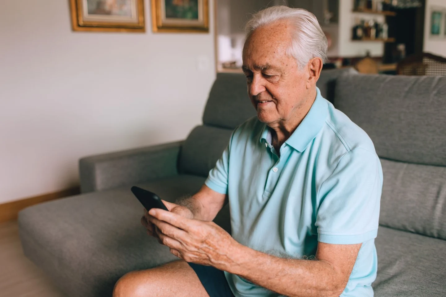 An older man holding his smartphone at home